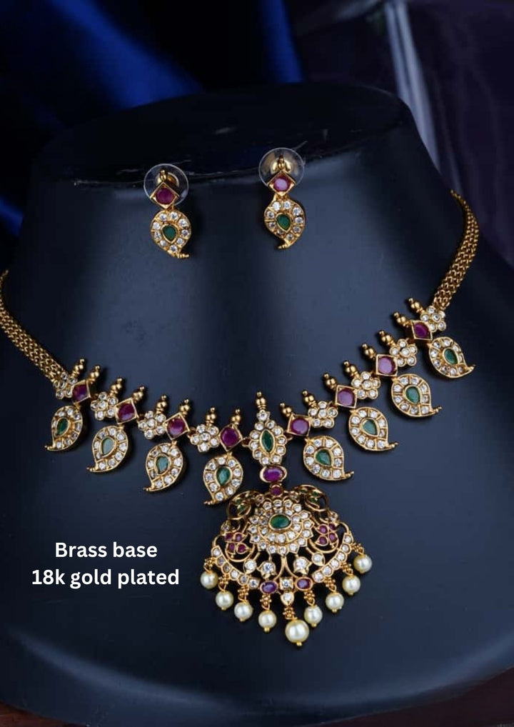 Traditional brass base 18K gold plated necklace set featuring detailed gold motifs, emerald and ruby stones, zircon embellishments, a statement pendant, pearl drops, and matching earrings.