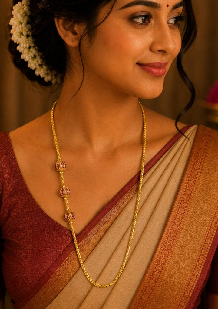 A south indian woman wearing a 18K gold plated thalli chain featuring beautifully crafted ruby designer bead accents with an elegant woven chain. Perfect for festive occasions and daily elegance.