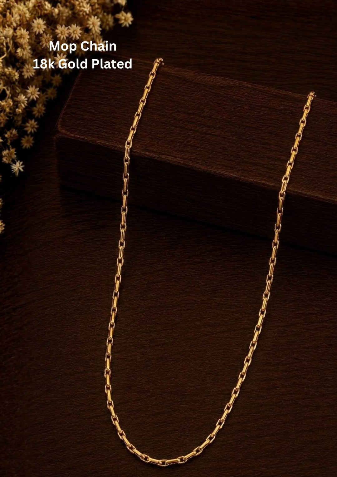 An elegant, sleek 18k gold-plated Mop chain displayed over a textured dark wooden surface. The chain features a continuous, sophisticated pattern of repeating cylindrical bar links seamlessly interconnected with small circular loops, offering a clean and polished modern look. Perfect for daily wear or for pairing with your favorite pendant.