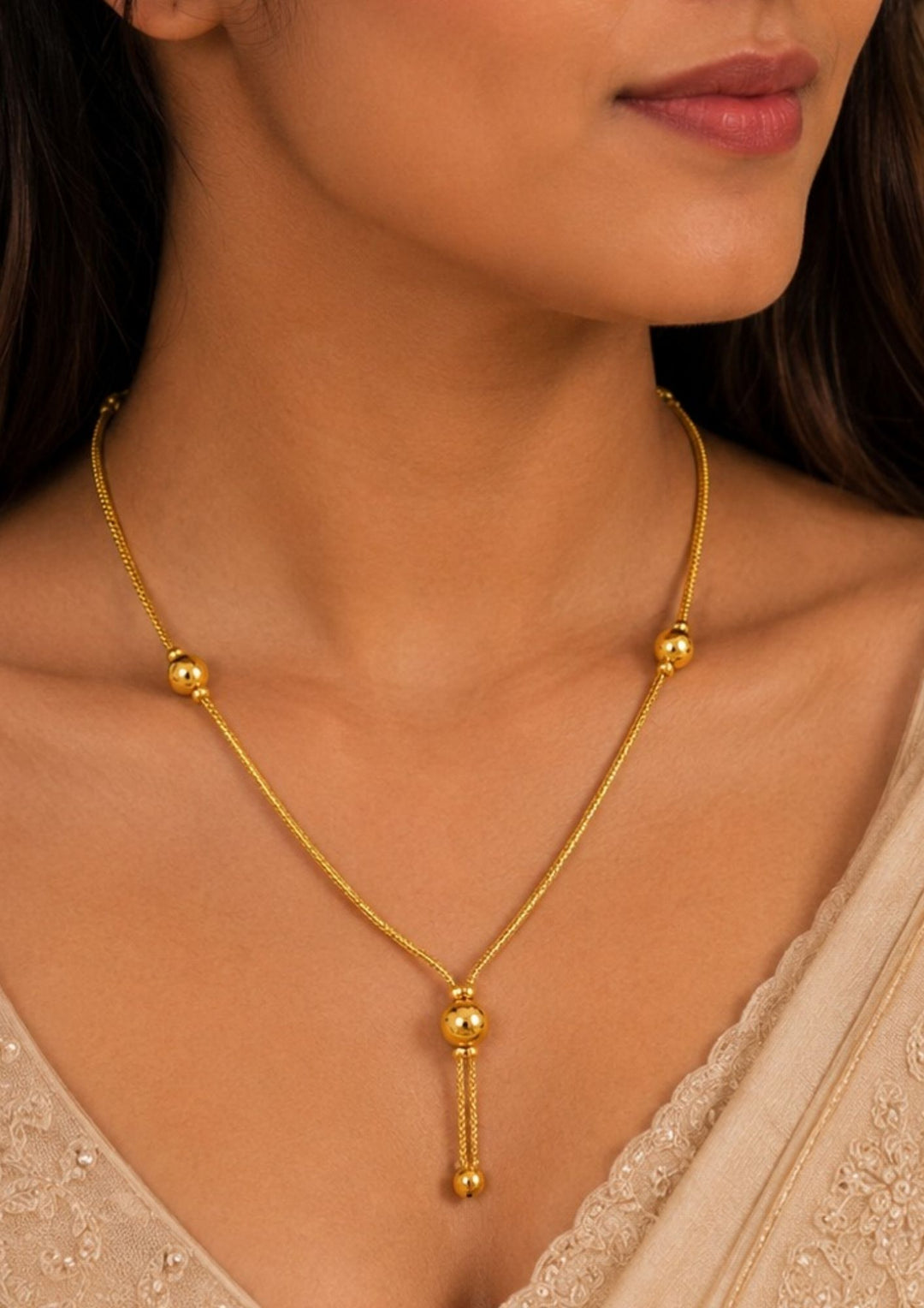 South indian Women wearing A sleek and minimalist 18k gold plated festive chain necklace featuring a delicate woven rope link. The chain is interspersed with small, polished gold spheres that guide the eye down to a central Y-shaped drop accent, complete with a larger hanging metallic globe bead, perfect for functions, weddings