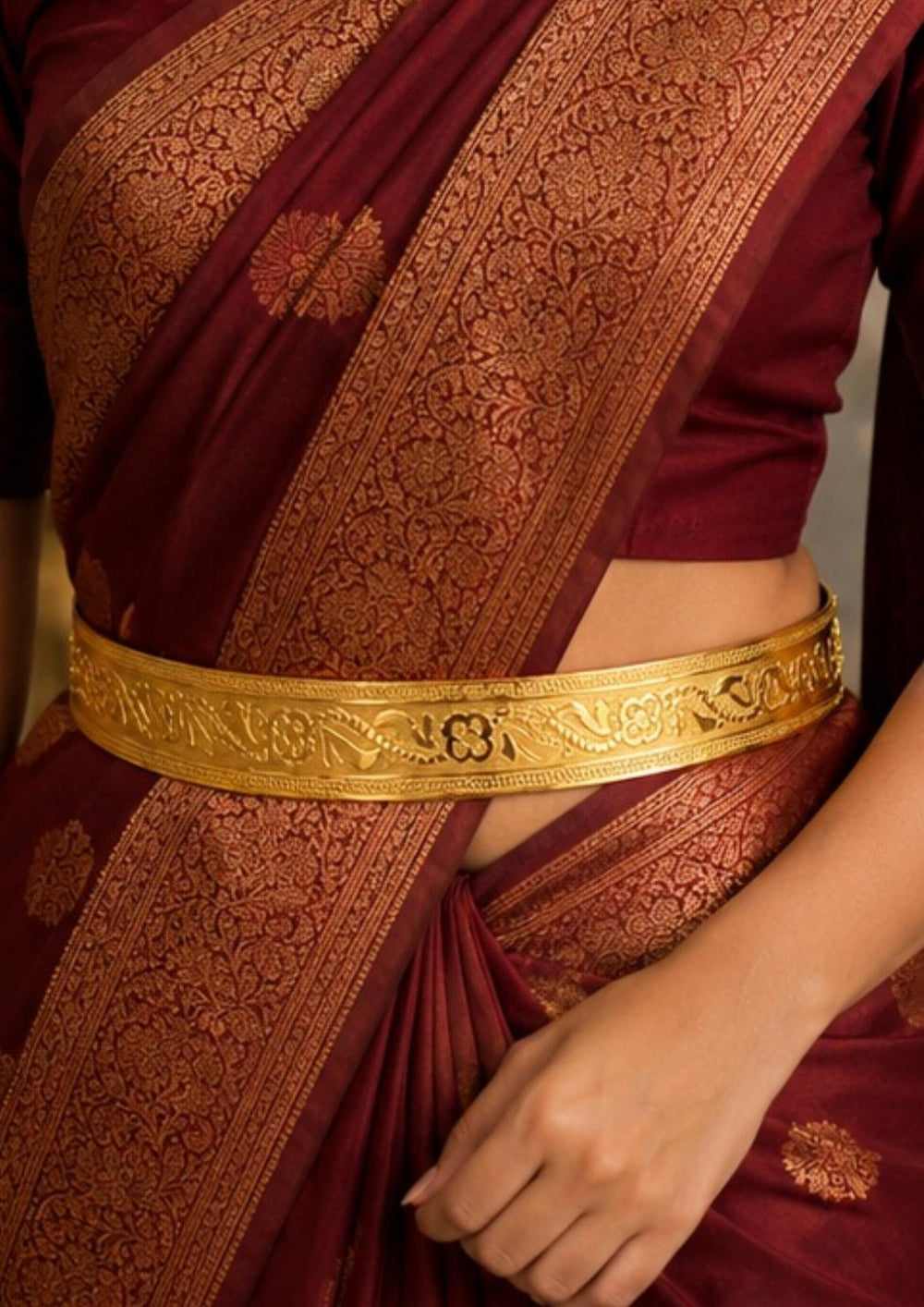 A close-up of a indian women wearing a traditional adult's hipbelt 18k gold plated waist hipbelt. The belt displays a polished high-shine inner surface and a beautifully embossed outer band featuring repeating floral and vine relief patterns.