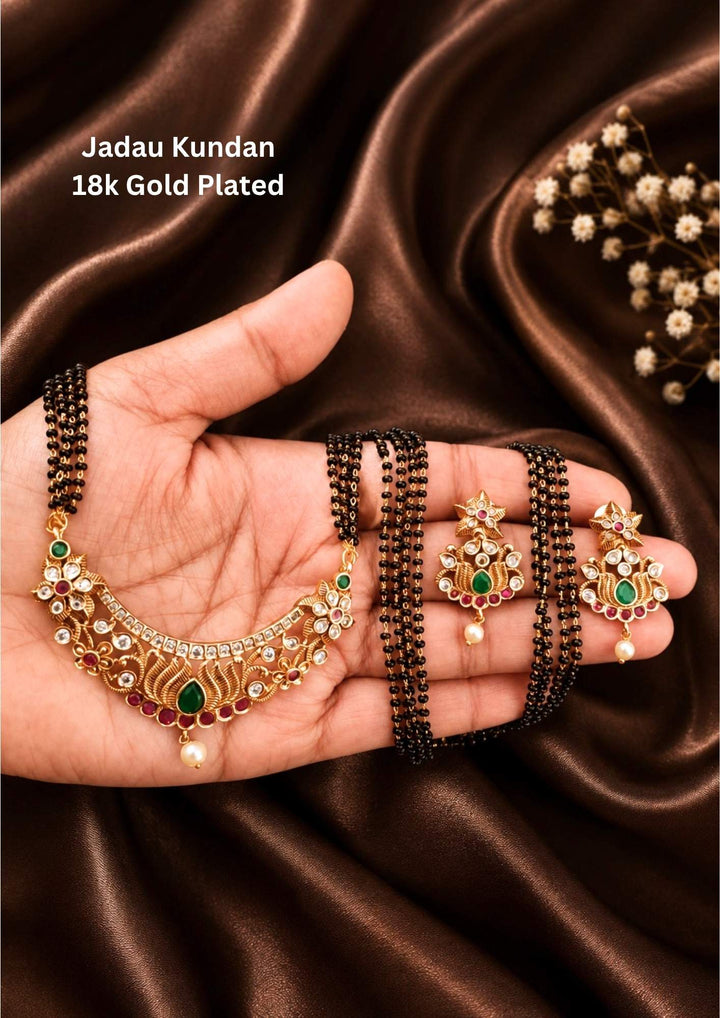 18k gold plated mangalsutra with designed by jadau kundan and with 5 rows of nallapusalu with matching earings that is with u shape and in lotus design with green emerald it is anti fade color and perfect for festivals, weddings and daily wear