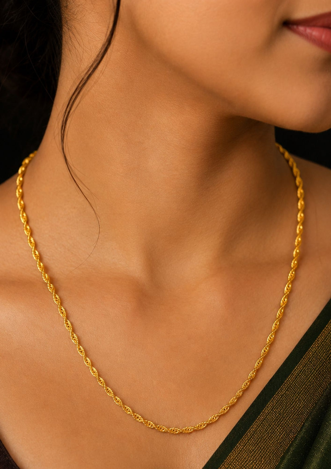 A close-up of a woman wearing a delicate gold chain necklace with a textured, twisted design. 