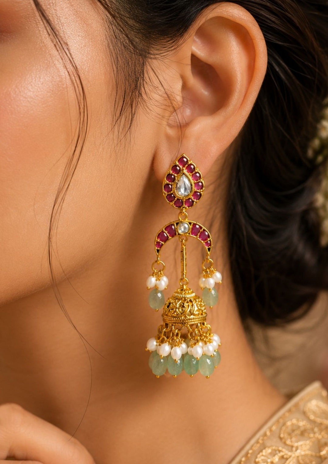 South Indian woman wearing ruby and green beads gold plated traditional jhumka earrings. The earrings showcase a classic temple-inspired design with sparkling kundan stones, pearl embellishments and hanging green beads, making them perfect for weddings, festive celebrations and ethnic wear.