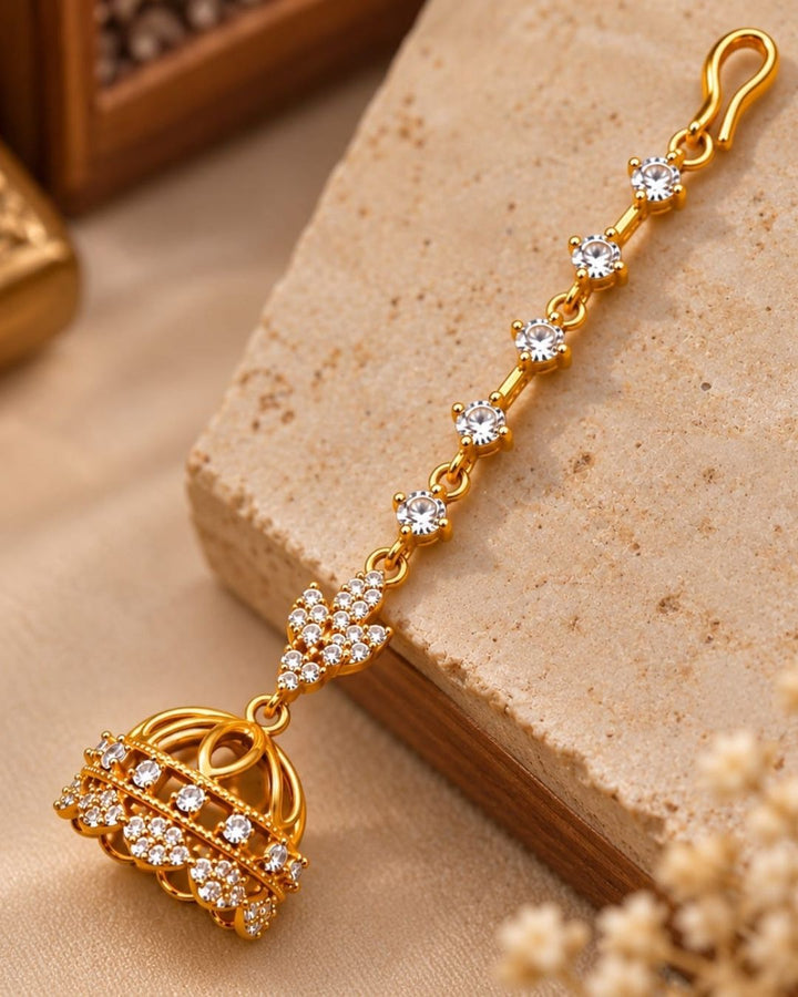 Traditional gold plated ear chain with matching jhumka earrings displayed against a carved wooden background with colourful floral accents.