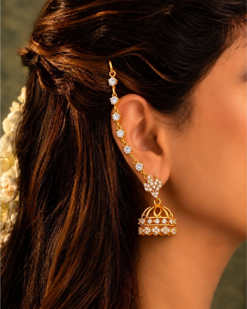 Traditional gold plated ear chain with matching jhumka earrings displayed against a carved wooden background with colourful floral accents.
