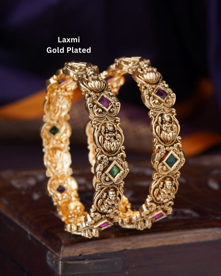 Traditional gold plated temple bangles with Goddess Lakshmi motifs, ruby pink and green square stones, and ornate antique-style craftsmanship.