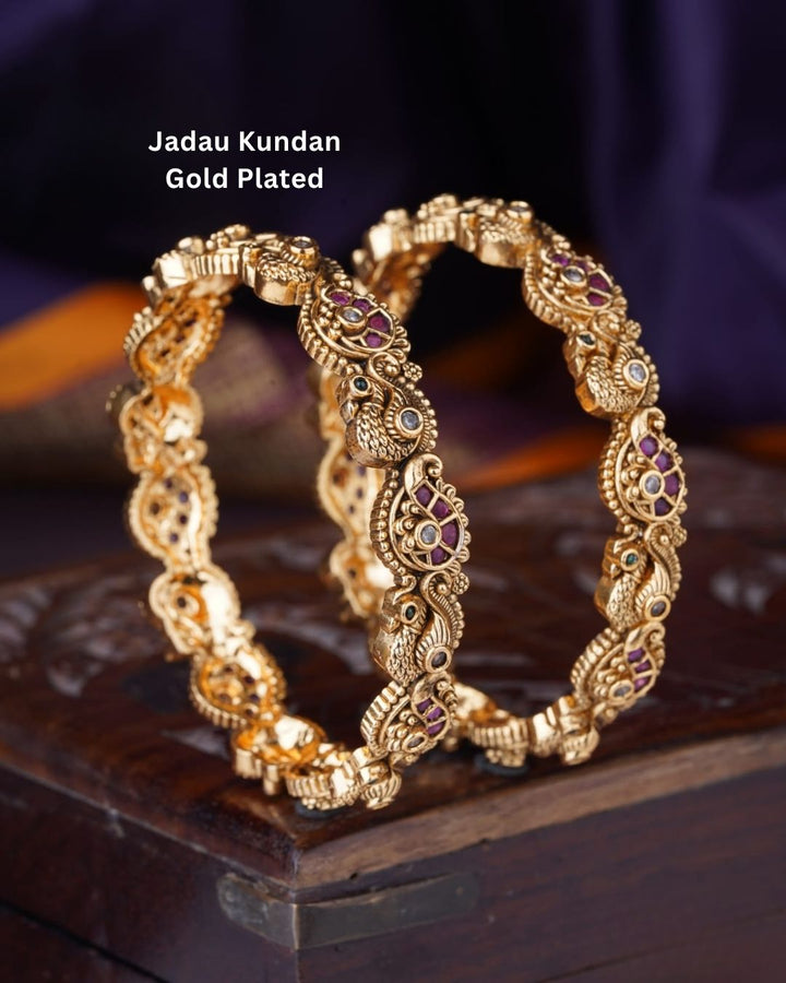Jadau kundan gold plated bangles featuring intricate peacock motifs, purple and green stone accents, and antique gold detailing.
