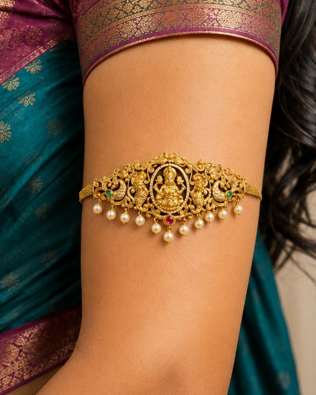 Premium gold plated 2-in-1 choker and bajuband featuring Goddess Lakshmi surrounded by intricate peacock and floral-inspired detailing, accented with green and pink stones and elegant pearl drops. Perfect for weddings, festive occasions, traditional wear, dance performances, parties and gifting.