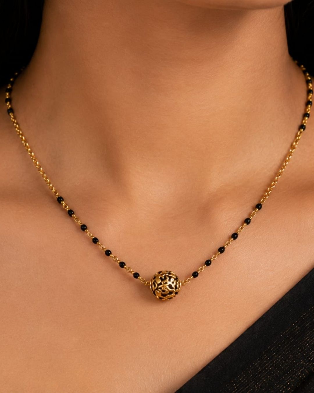 Gold replica black beads necklace featuring a delicate gold-toned chain, black beads, and a round textured gold pendant at the center, displayed on a maroon jewellery bust.