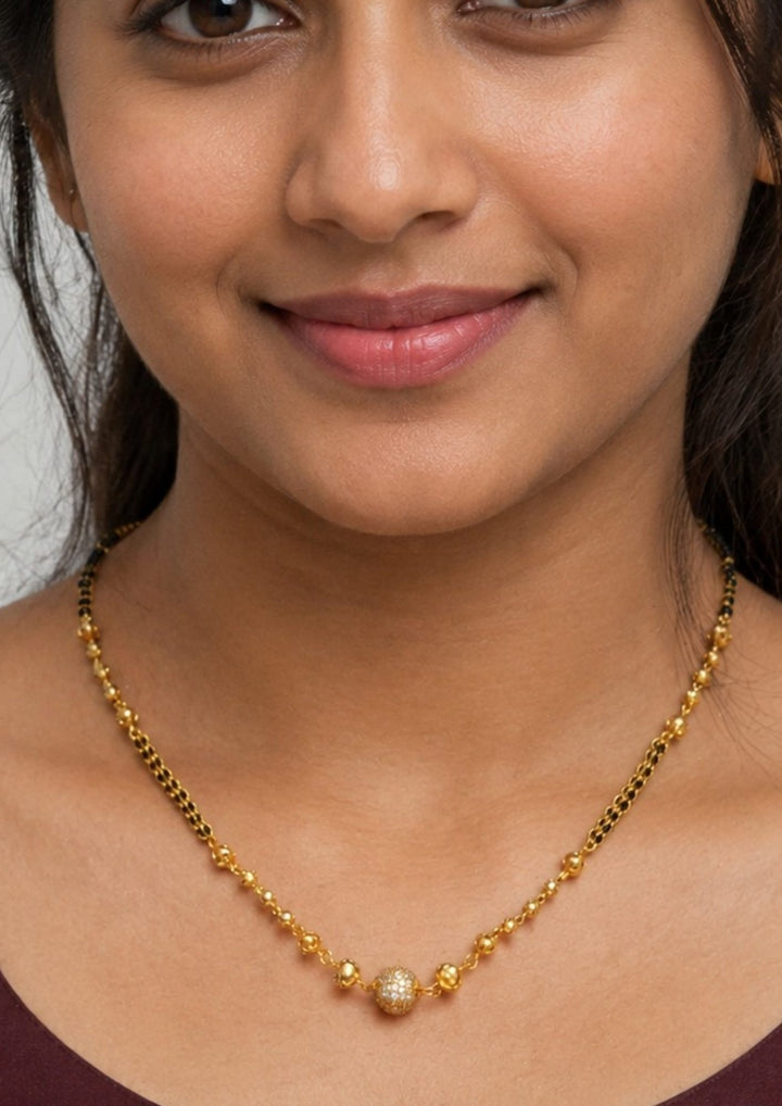 Woman wearing a gold plated necklace with gold plated Ball shape mangalsutra necklace The design features a delicate gold link chain transitioning into sections of traditional small black beads on both sides. The central pendant showcases a sleek, contemporary curved ball shape  and a stylized   . This elegant neckpiece perfect for daily wear, office wear, and casual outfits and weddings , festivals .