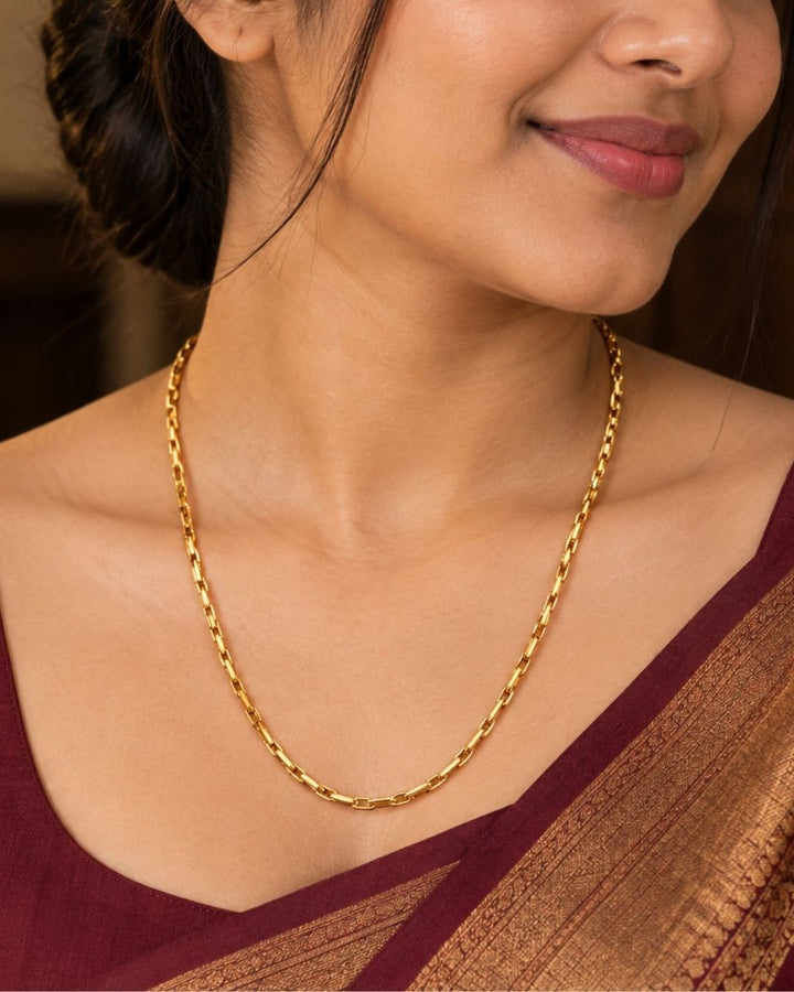 An elegant, sleek 18k gold-plated Mop chain displayed over a textured dark wooden surface. The chain features a continuous, sophisticated pattern of repeating cylindrical bar links seamlessly interconnected with small circular loops, offering a clean and polished modern look. Perfect for daily wear or for pairing with your favorite pendant.