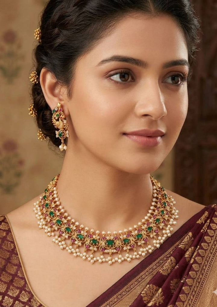south indian Woman wearing a traditional necklace and earrings Gold-plated necklace and earrings set with pearls and gemstones comes with jadau kundan and it comes with in detailed peacock design and  comes with pearl beads and looks traditional for weeding , functional 