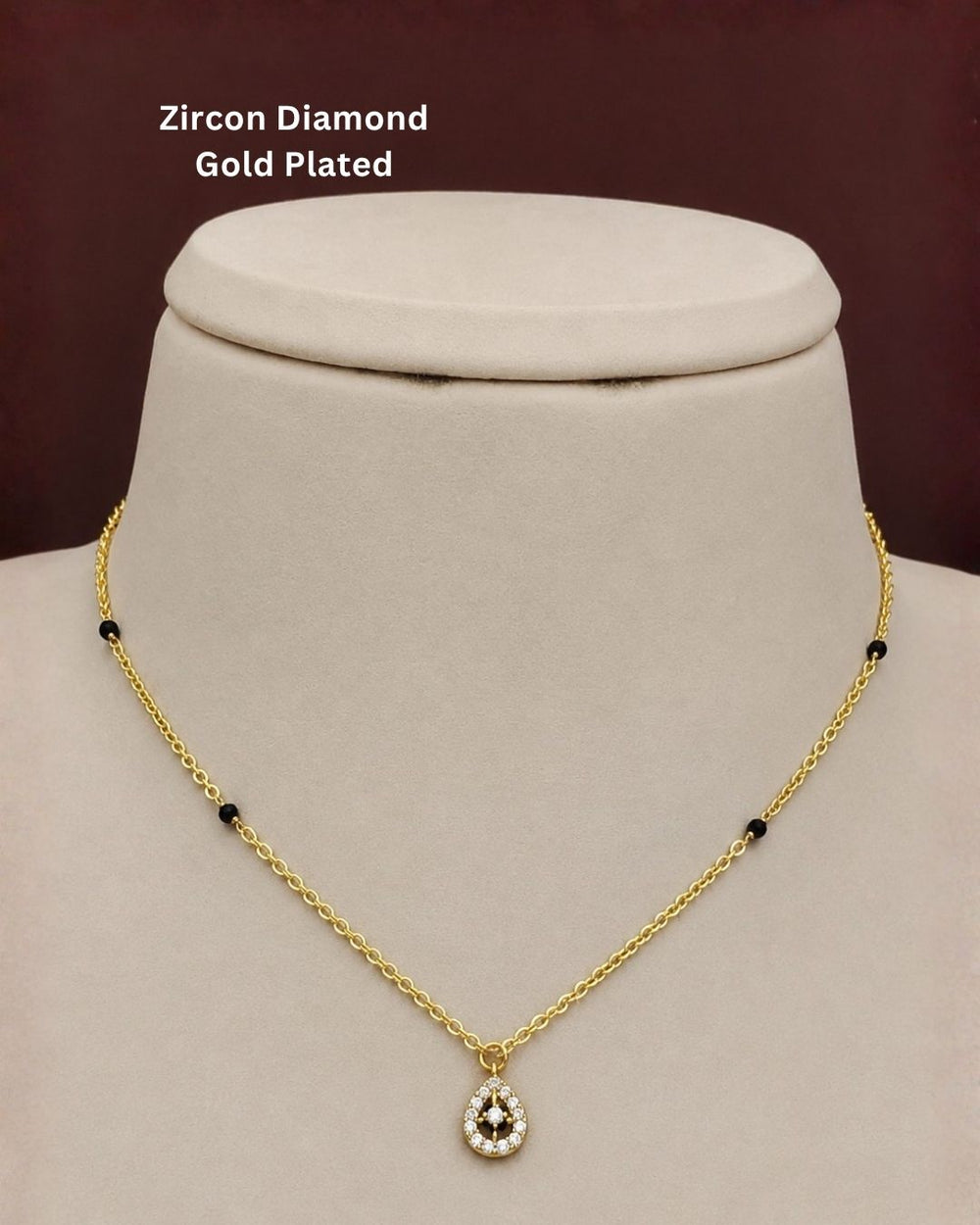 Gold-plated necklace with a teardrop-shaped zircon pendant and small black bead accents, displayed on a cream jewelry bust against a dark brown background. Text overlay reads 'Zircon Diamond Gold Plated'.
