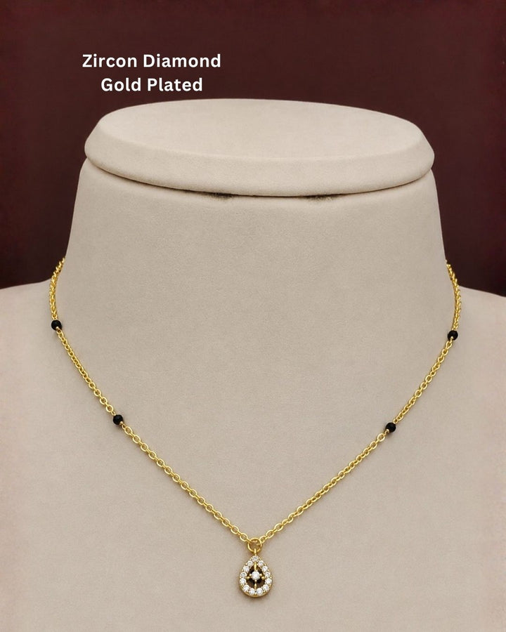 Gold-plated necklace with a teardrop-shaped zircon pendant and small black bead accents, displayed on a cream jewelry bust against a dark brown background. Text overlay reads &