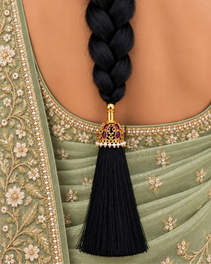 Traditional gold plated hair accessory featuring an ornate dome-shaped design with ruby-colored stones, pearl detailing, a long black tassel, and a decorative black cord, perfect for festive and traditional hairstyles.