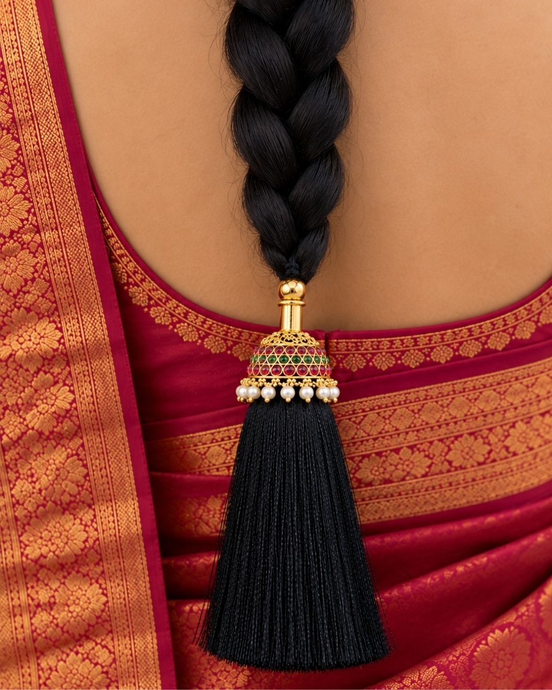Elegant gold plated Jada Gantalu featuring a dome-shaped design with ruby and green stones, delicate pearl drops, and a long black thread tassel, perfect for bridal and festive hairstyles.