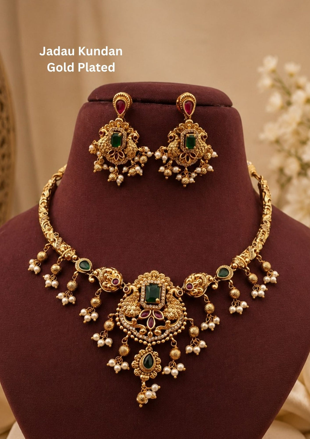 An exquisite Jadau Kundan gold plated necklace features a rigid gold-engraved band transitions into twin peacock motifs framing a central rectangular green emerald stone, accented by delicate hanging pearl clusters and matching drop earrings.
