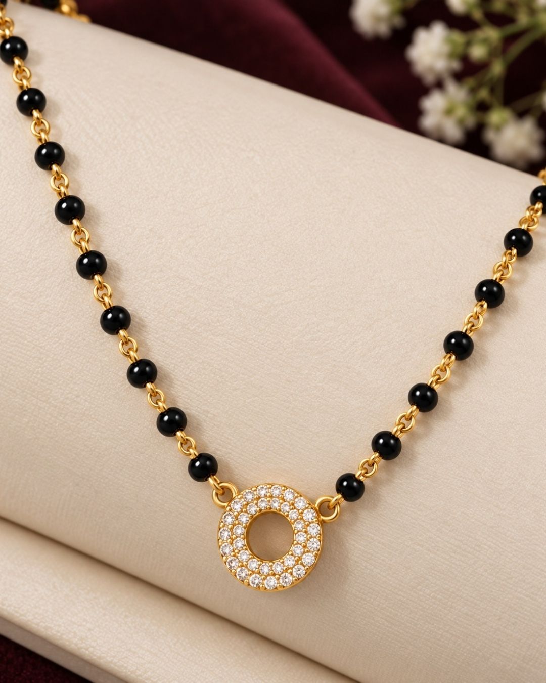 South indian Women wearing Gold plated black bead mangalsutra with a circular stone pendant displayed on a beige surface with a minimal decorative background.