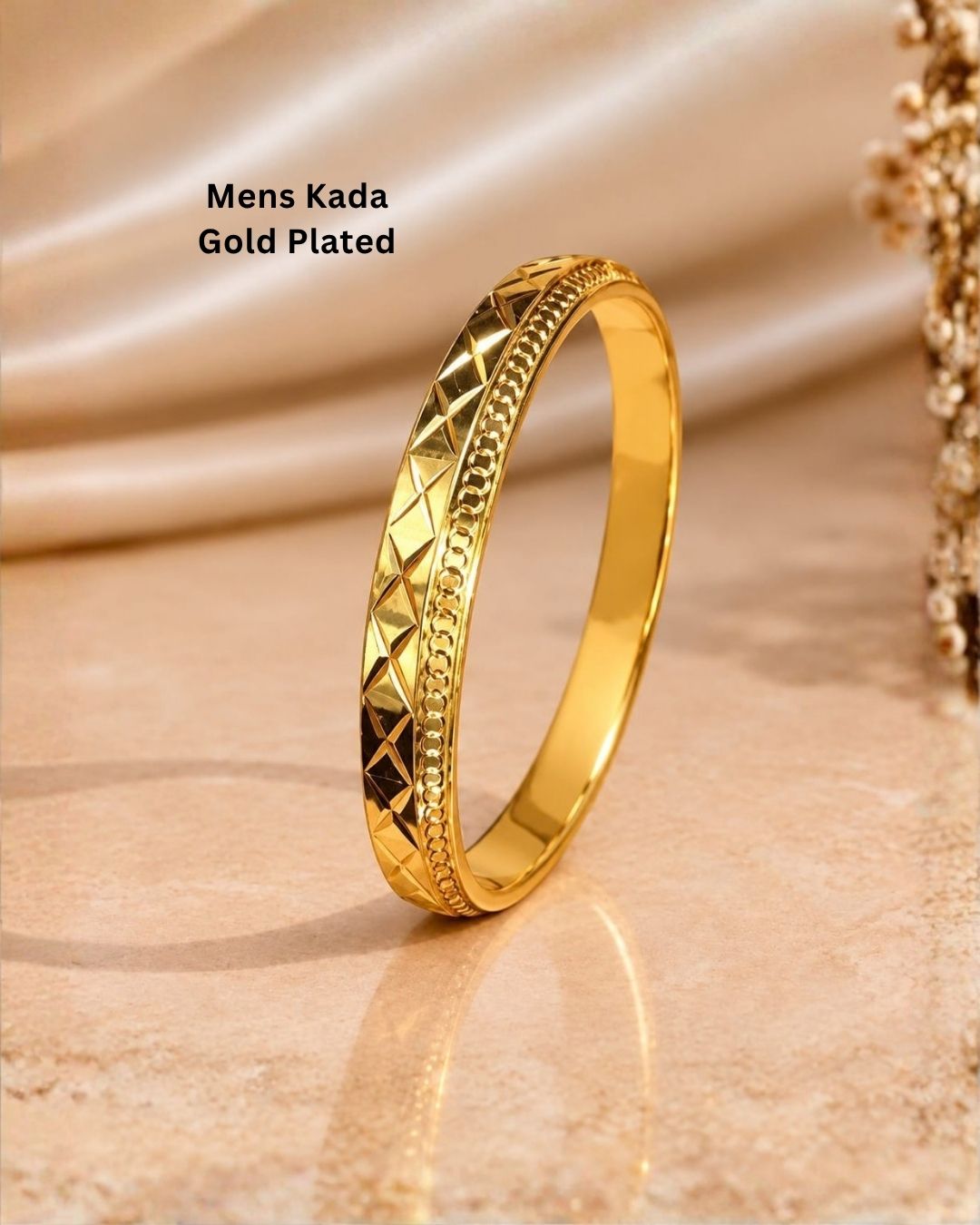 Gold plated men’s kada displayed upright on a warm beige surface, showcasing its diamond-cut design and glossy finish.