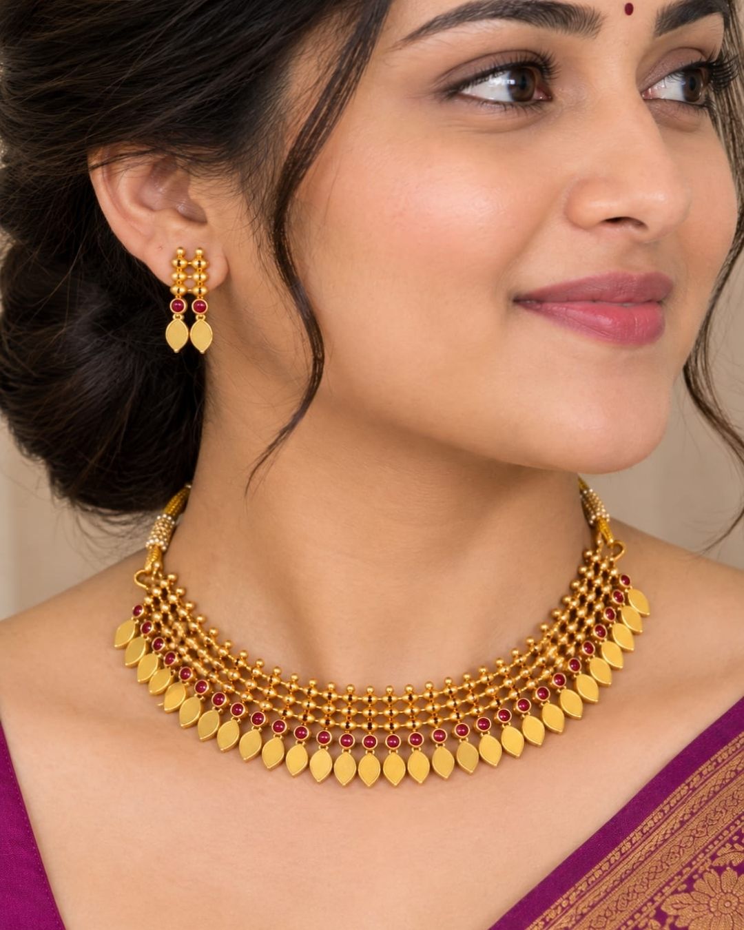 Premium gold plated Elakathaali necklace set featuring intricate traditional beadwork, red stone accents, and a row of elegant leaf-shaped motifs, paired with matching earrings. Perfect for weddings, festive occasions, traditional wear, parties, and gifting.