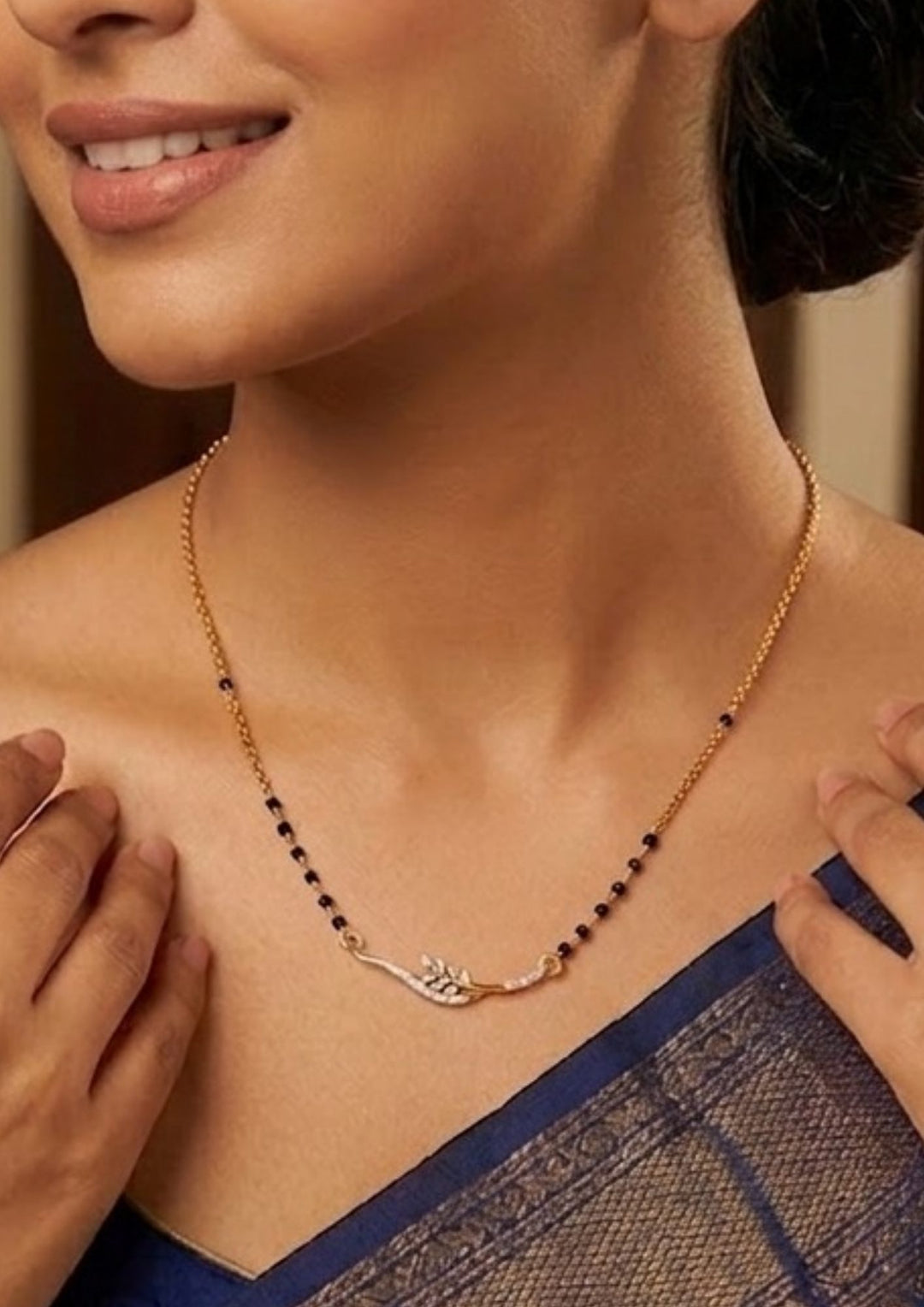 Woman wearing a gold necklace with black beads, close-up of the necklace Modern Zircon Diamond gold plated mangalsutra necklace The design features a delicate gold link chain transitioning into sections of traditional small black beads on both sides. The central pendant showcases a sleek, contemporary curved V-shape and a stylized butterfly or floral motif encrusted with sparkling white cubic zirconia stones. This elegant neckpiece perfect for daily wear, office wear, and casual outfits.