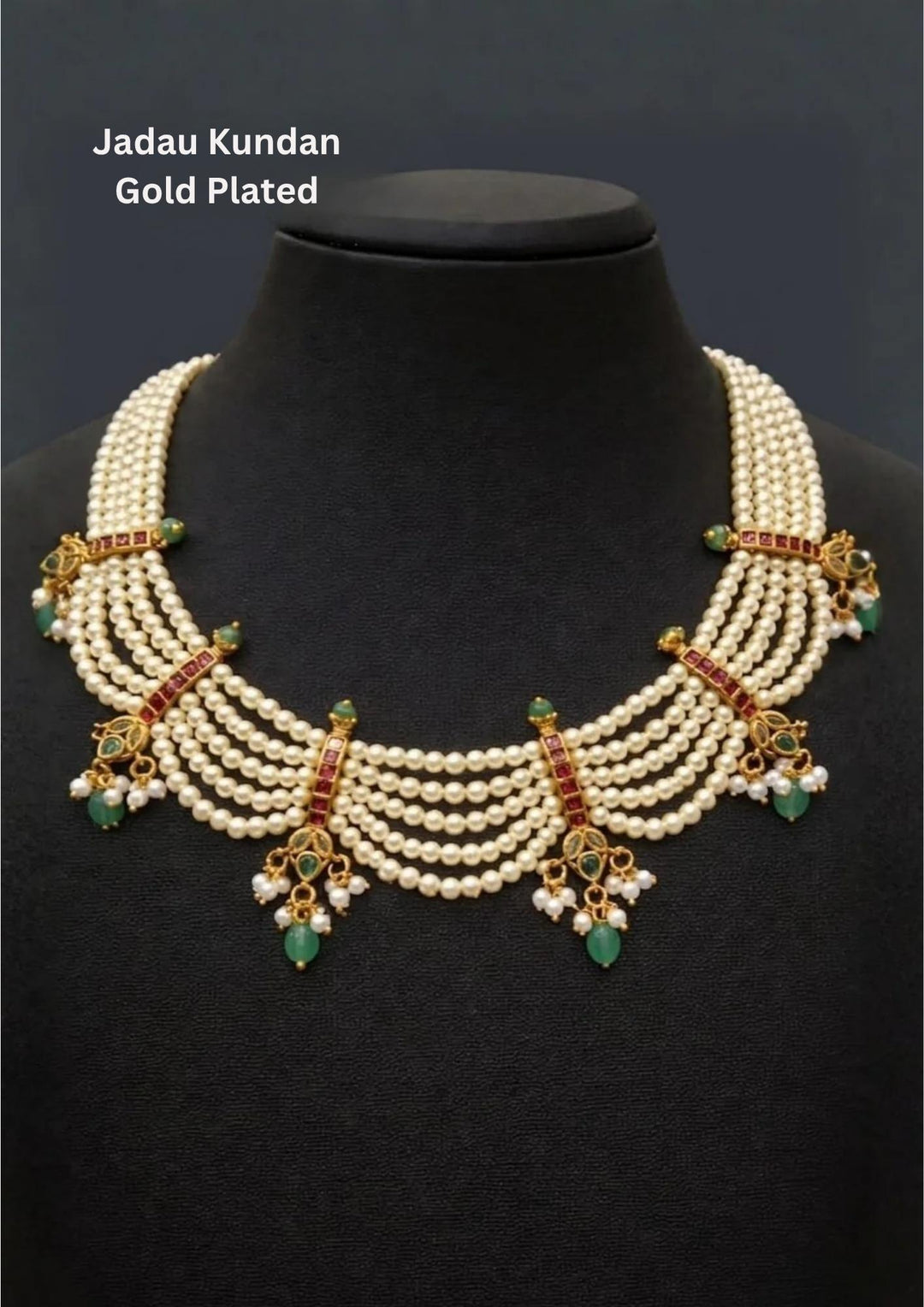 A grand gold plated festive choker necklace meticulously hand-strung with five parallel tiers of smooth cream white rice pearls. The layered strands are joined by intricate vertical gold bars inlaid with red ruby squares and finish in dainty scalloped drapes accented by hanging green teardrop emerald beads and tiny pearl cluster bunches.