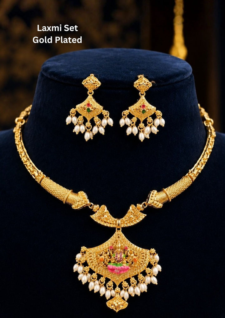 A traditional temple-style gold-plated choker necklace set featuring Goddess Laxmi. The central fan-shaped pendant beautifully displays a seated Goddess Laxmi motif accented with pink and green enamel work, connected to a textured rigid collar chain and finished with elegant hanging white pearl drops. Perfect for for bridal and festive wear. It is anti tarnish and skin friendly