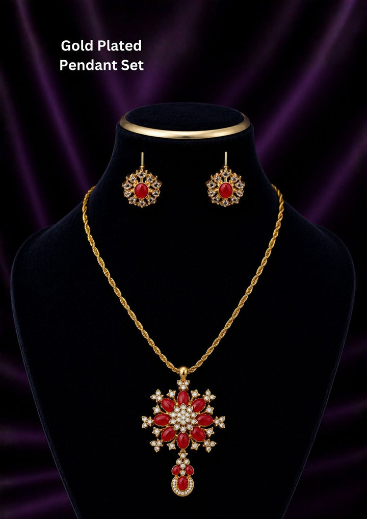 Gold plated pendant necklace and matching stud earrings displayed on a black velvet jewelry bust against a dark purple draped background. The necklace features a large red and white floral pendant with a teardrop drop, and the matching earrings are shown above the bust.