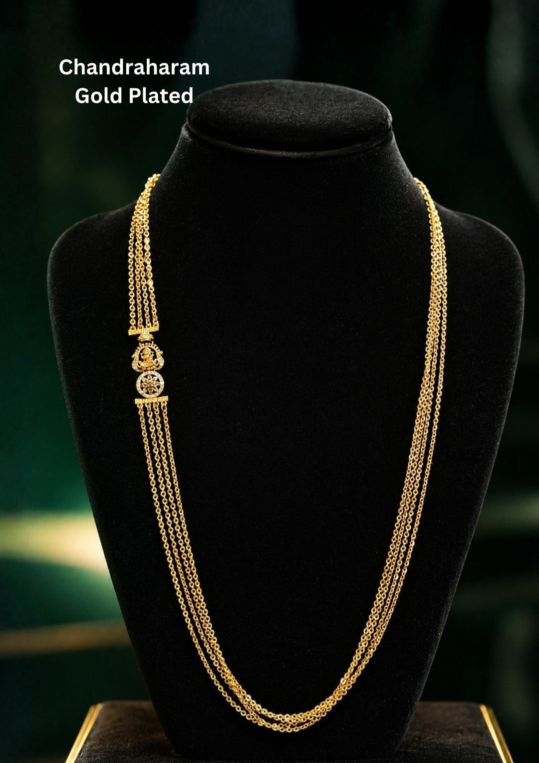 A traditional brass base gold plated haram necklace featuring a multi-strand design with four layers of delicate link chains. The side is elegantly accented with a small, traditional round medallion brooch encrusted with ruby, emerald, and white stone details, beautifully presented on a black velvet display bust.