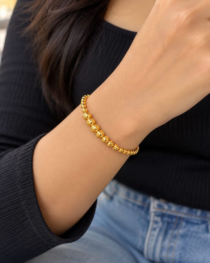 Beautiful gold plated beaded bracelet featuring a sequence of intricately textured round beads, delicate chain detailing, and a polished finish. Perfect for everyday wear, festive occasions, traditional outfits, parties, and gifting.