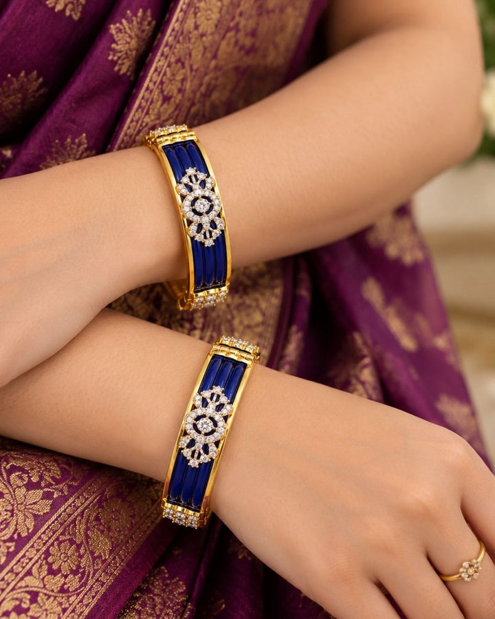Designer gold plated bangles featuring deep blue detailing, sparkling white stone floral motifs, and polished gold borders, perfect for festive, wedding, traditional, and special occasions.