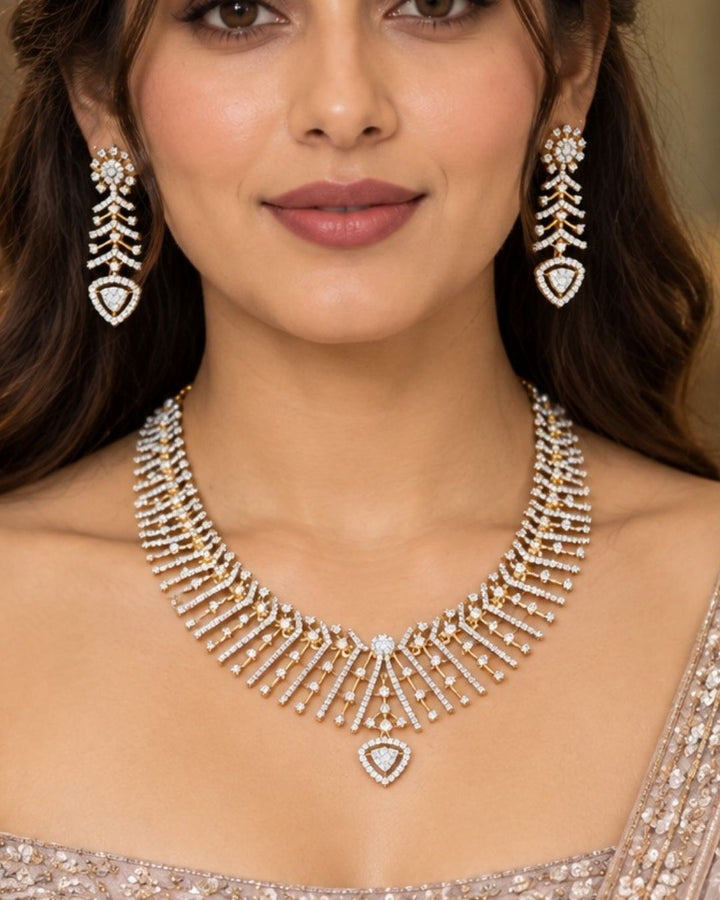South Indian Women wearing gold plated V-shaped collar necklace with a modern Art Deco aesthetic. The structured necklace features alternating diagonal bars encrusted with micro pure Zirconian diamonds, creating a shimmering chevron fringe that culminates in a central teardrop crystal pendant, complete with matching drop earrings.