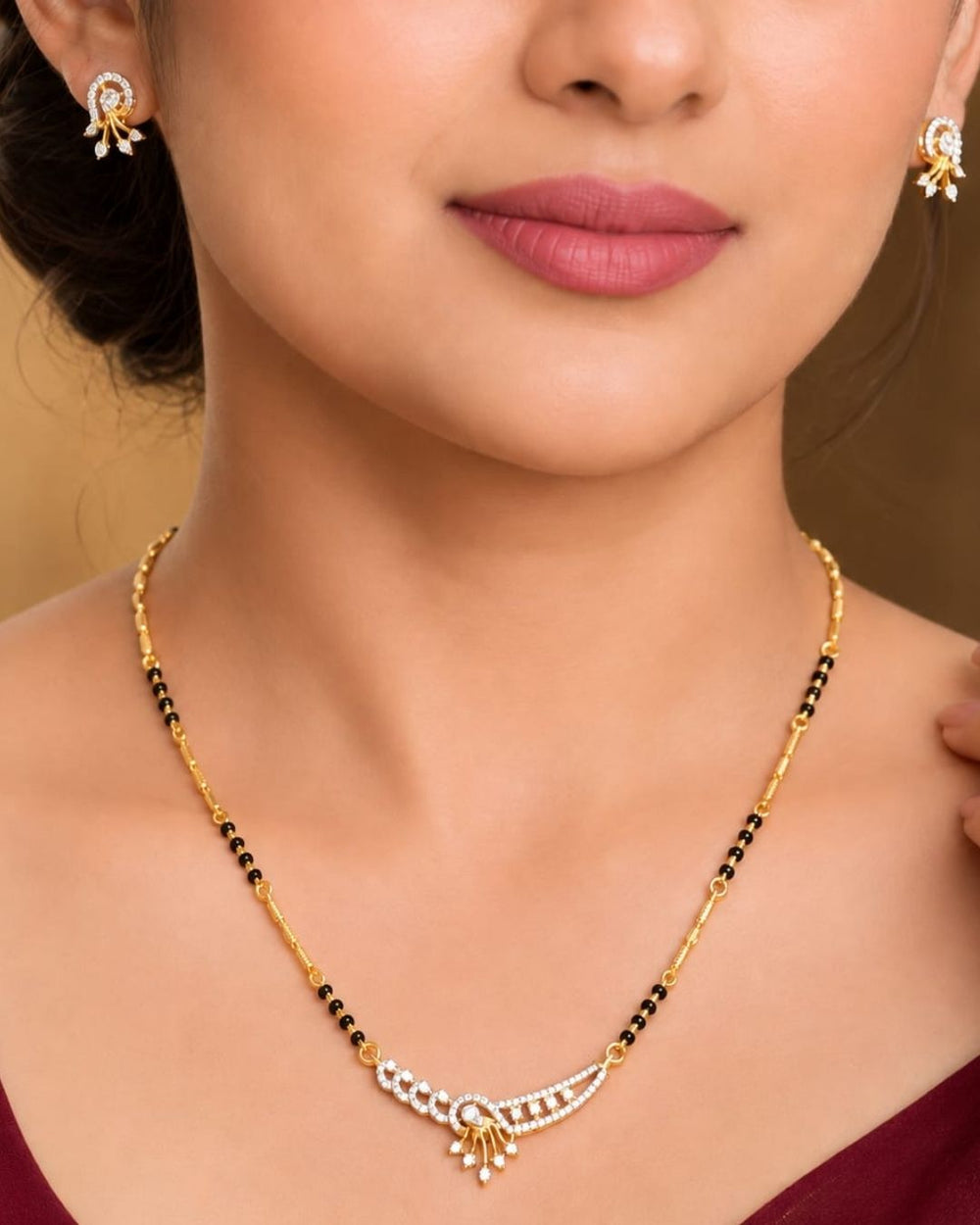 A close-up of a woman wearing a gold and black beaded necklace with a silver and white stone pendant, along with matching stud earrings.
