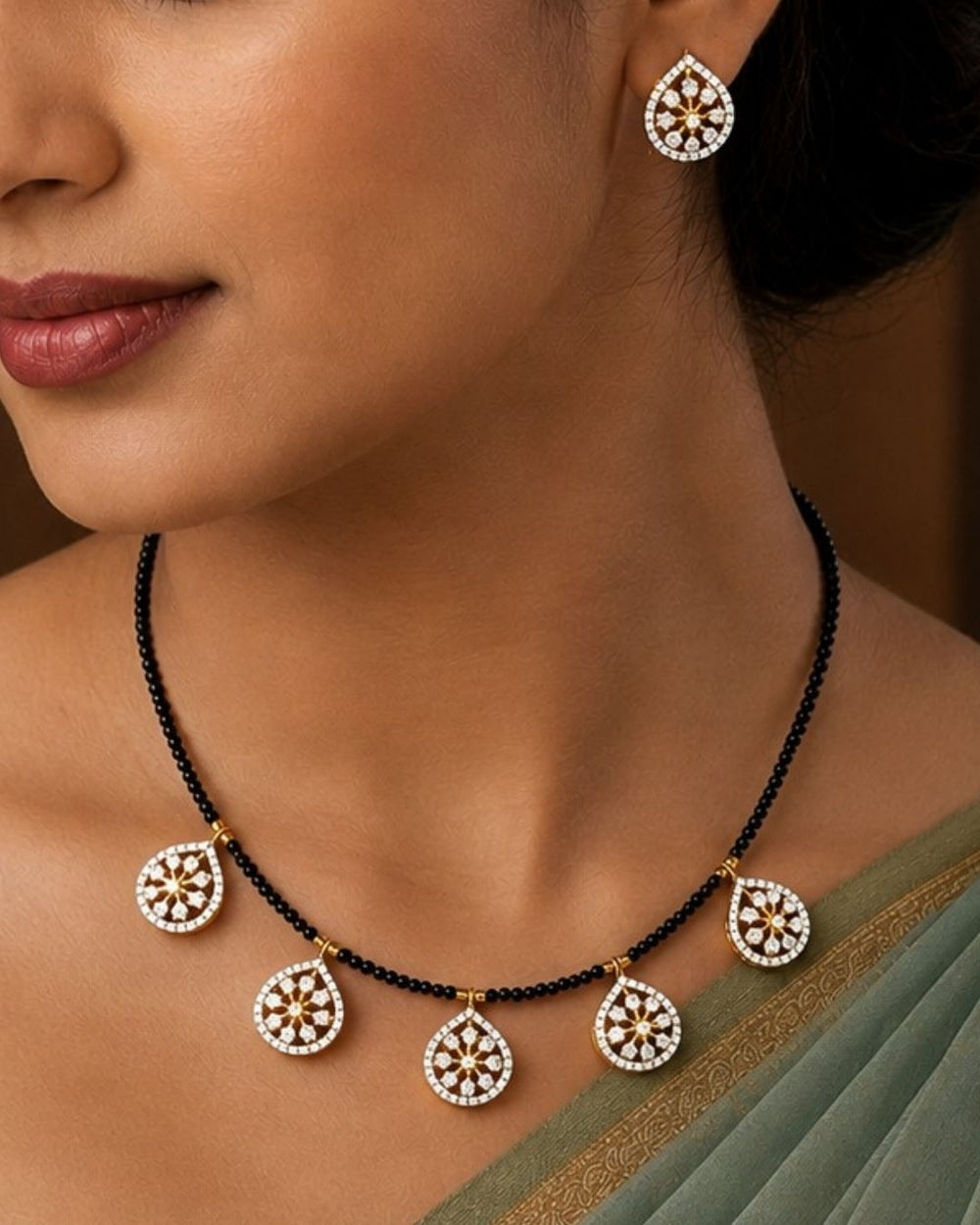 A close-up of a south indian woman wearing a black beaded necklace with five ornate gold and white teardrop-shaped pendant charms, along with matching drop earrings.