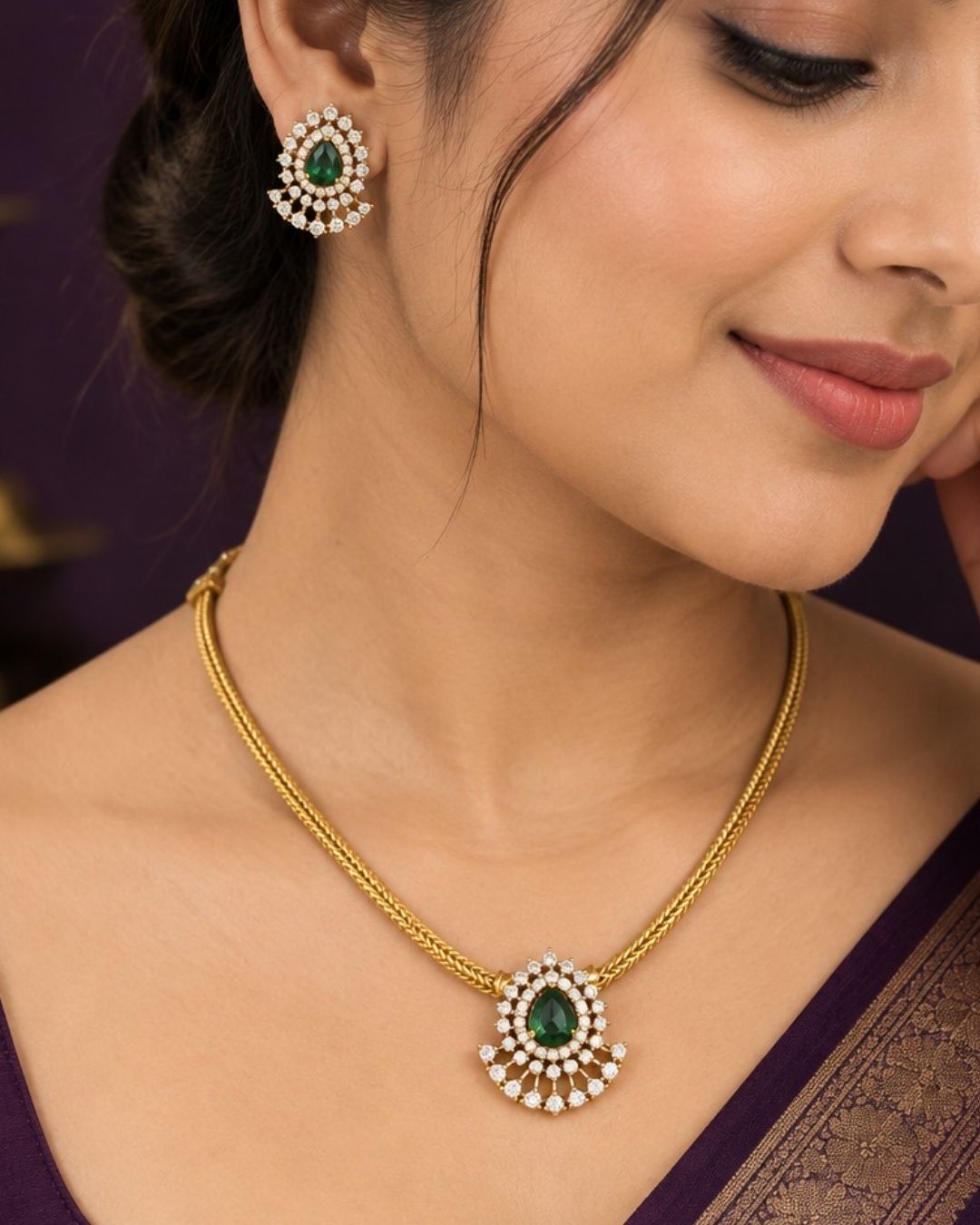 A minimalist 18k gold plated herringbone chain necklace featuring a central teardrop-shaped ruby green stone. The stone is enclosed in a halo of white pure Zircon diamonds that flares out at the bottom into a shimmering, fan-shaped scalloped fringe, paired with matching crown-set ear studs.