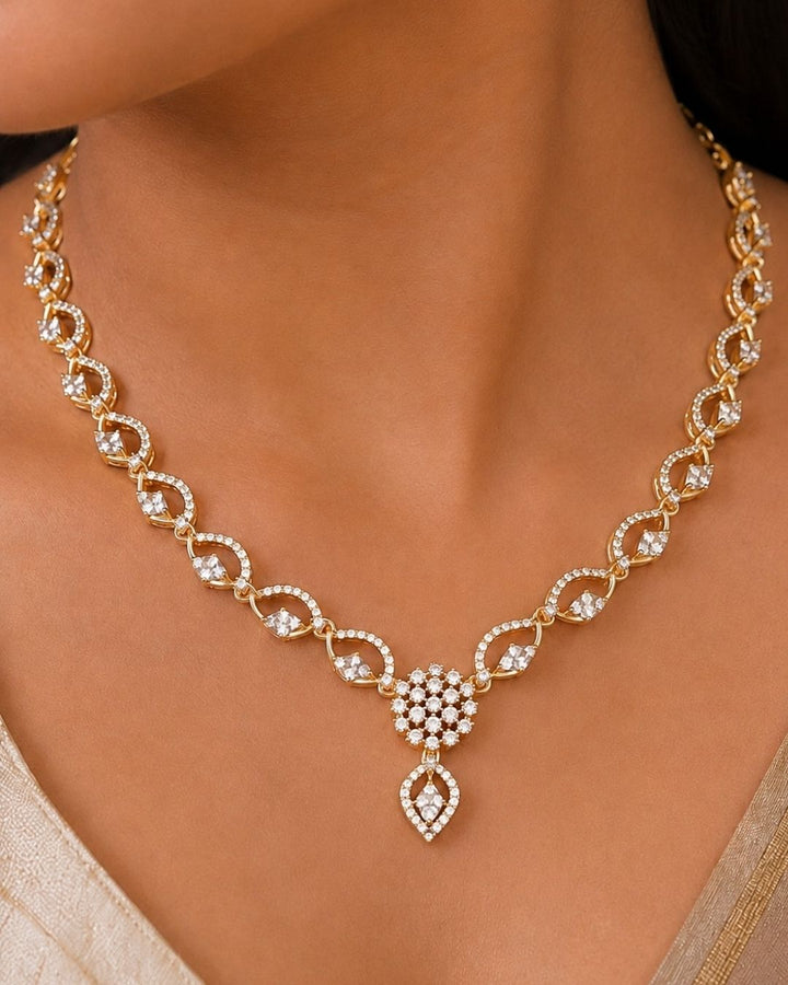 Beautiful gold plated necklace set featuring repeating loop-shaped links embellished with sparkling stones, a floral-inspired pendant, and matching drop earrings. Perfect for traditional wear, festive occasions, weddings, parties, and gifting.