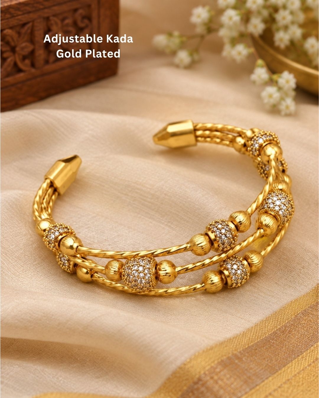 Gold plated adjustable kada for women featuring a triple twisted design, decorative gold beads, and sparkling white stone embellishments.