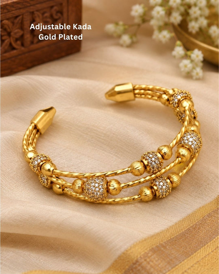 Gold plated adjustable kada for women featuring a triple twisted design, decorative gold beads, and sparkling white stone embellishments.