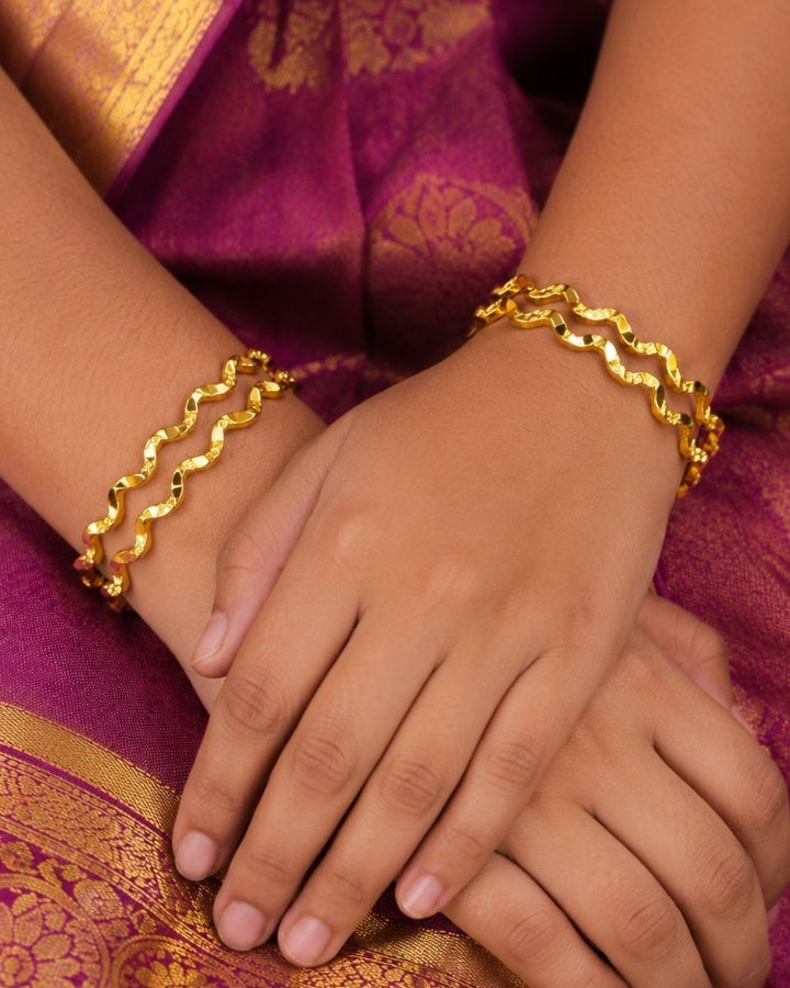Four gold-plated spiral bangles displayed together on a dark textured surface, with white text in the upper left reading &