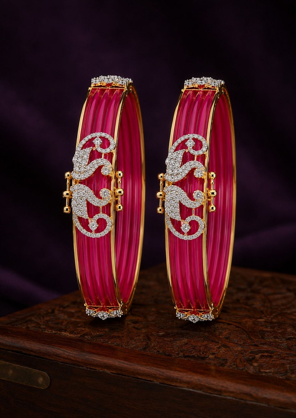 A pair of traditional Indian bangles with vibrant magenta pink ribbed enamel, gold-plated borders, and intricate silver paisley motifs embellished with clear stones. Perfect for weddings, festive occasions, traditional wear, parties, and everyday styling. 