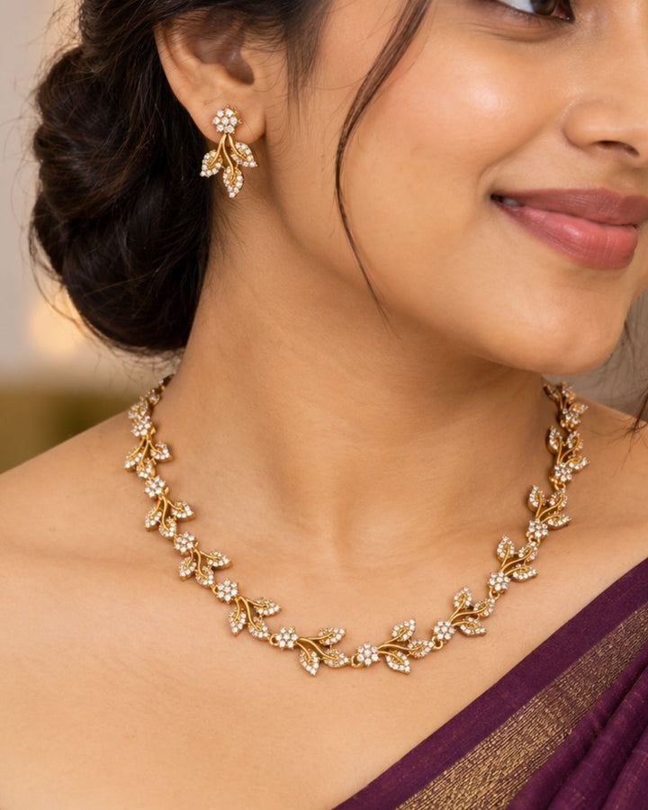 Designer gold plated necklace and earrings set featuring an elegant arrangement of leaf and floral motifs embellished with sparkling white stones, perfect for festive, wedding, and elegant occasions.