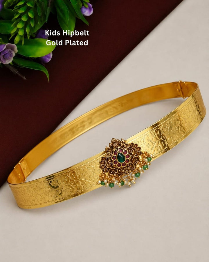 Beautiful gold plated kid’s hip belt featuring a wide intricately engraved band with a floral gemstone centerpiece decorated with ruby, green stones, and pearl drops. Perfect for children’s traditional wear, weddings, festive occasions, cultural events, parties, and gifting.