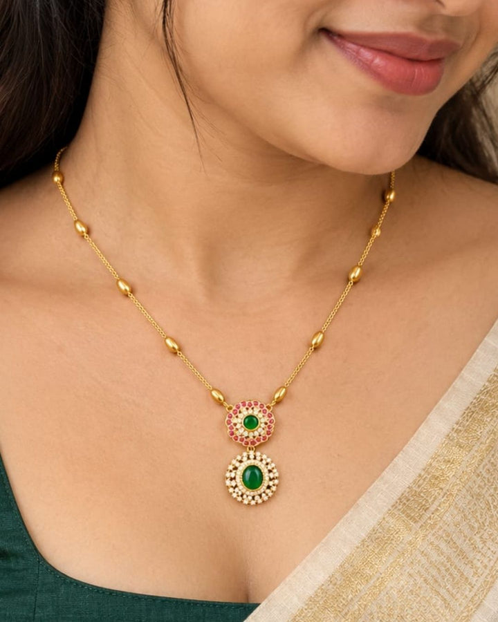 Traditional gold plated designer necklace featuring a delicate beaded chain and an elegant double green stone pendant with ruby-colored and white stone accents.