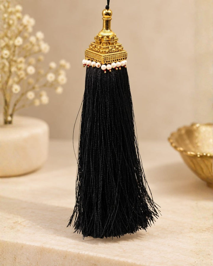 Elegant gold plated Jada Gantalu featuring a detailed temple-style design, white pearl accents, red bead detailing, and long flowing black tassels, perfect for traditional occasions and bridal looks.