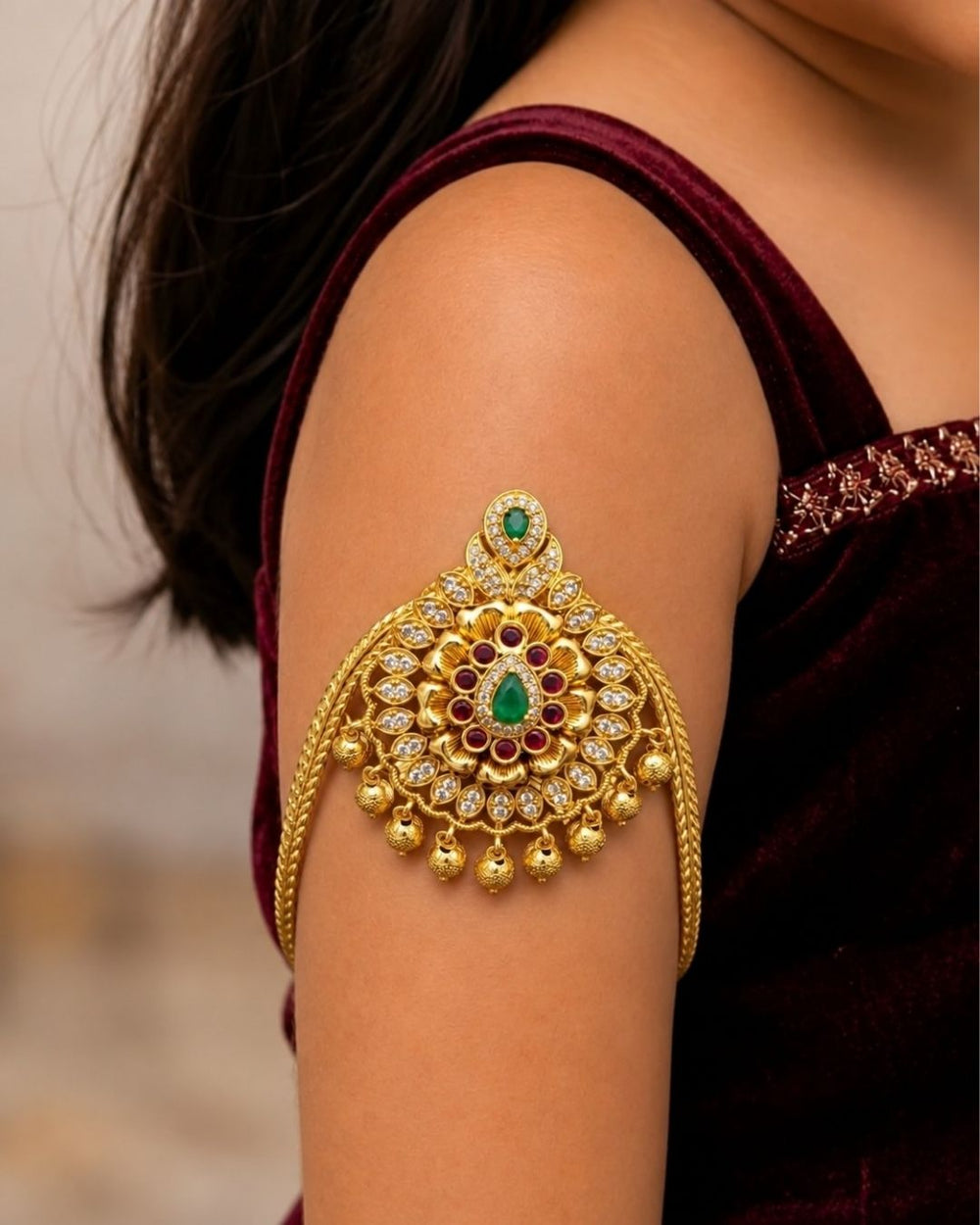 Premium gold plated baby vanki featuring an ornate floral motif with green and ruby-colored stone detailing, sparkling accents, and delicate hanging gold beads. Perfect for baby girls, traditional occasions, weddings, festivals, and gifting.