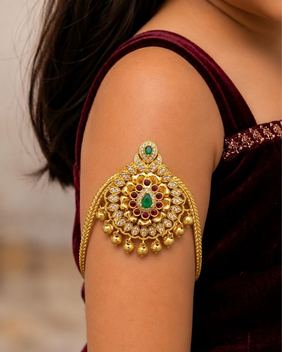 Premium gold plated baby vanki featuring an ornate floral motif with green and ruby-colored stone detailing, sparkling accents, and delicate hanging gold beads. Perfect for baby girls, traditional occasions, weddings, festivals, and gifting.