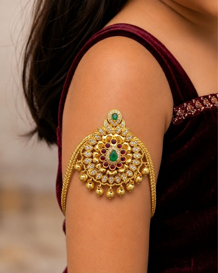 Premium gold plated baby vanki featuring an ornate floral motif with green and ruby-colored stone detailing, sparkling accents, and delicate hanging gold beads. Perfect for baby girls, traditional occasions, weddings, festivals, and gifting.