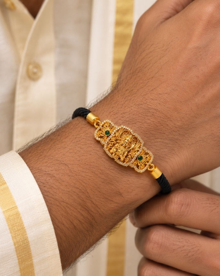 Traditional gold plated men’s bracelet featuring an intricately detailed Lord Hanuman centerpiece, black twisted thread band, sparkling stone borders, green stone accents, and adjustable detailing, perfect for spiritual, traditional, and everyday wear.