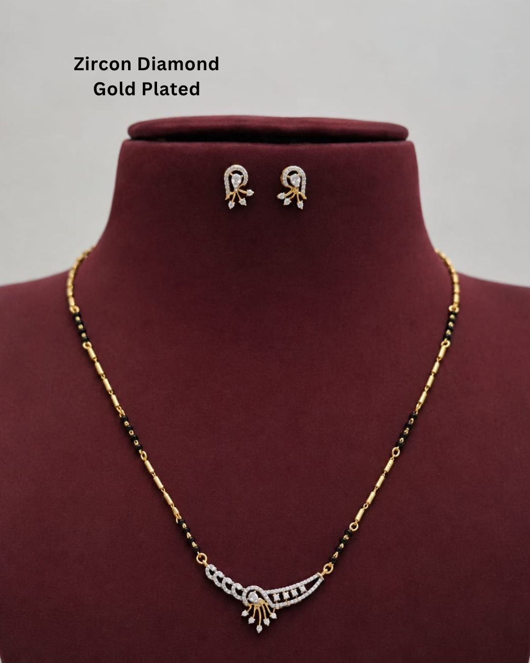 Gold-plated zircon diamond necklace and matching stud earrings displayed on a dark red jewelry bust. The necklace features a gold-plated curved pendant with clear stones and black beads along the chain.